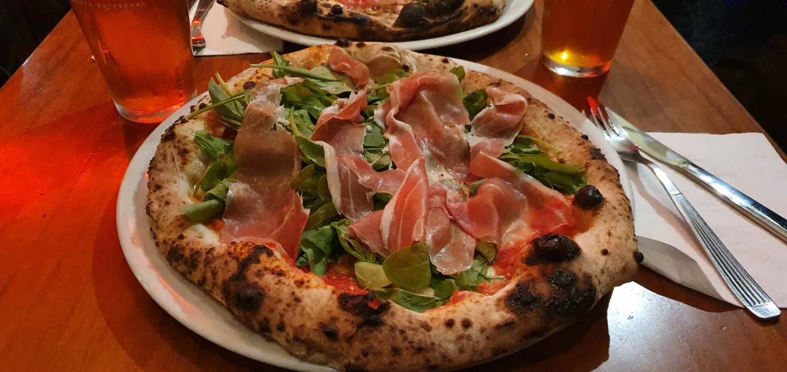 Pizza napolitana con jamón crudo y rúcula, borde aireado y leopardo, servida en la mesa